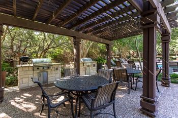 an outdoor kitchen and dining area under a pergola with trees in the background at Sonterra Apartment Homes, Texas